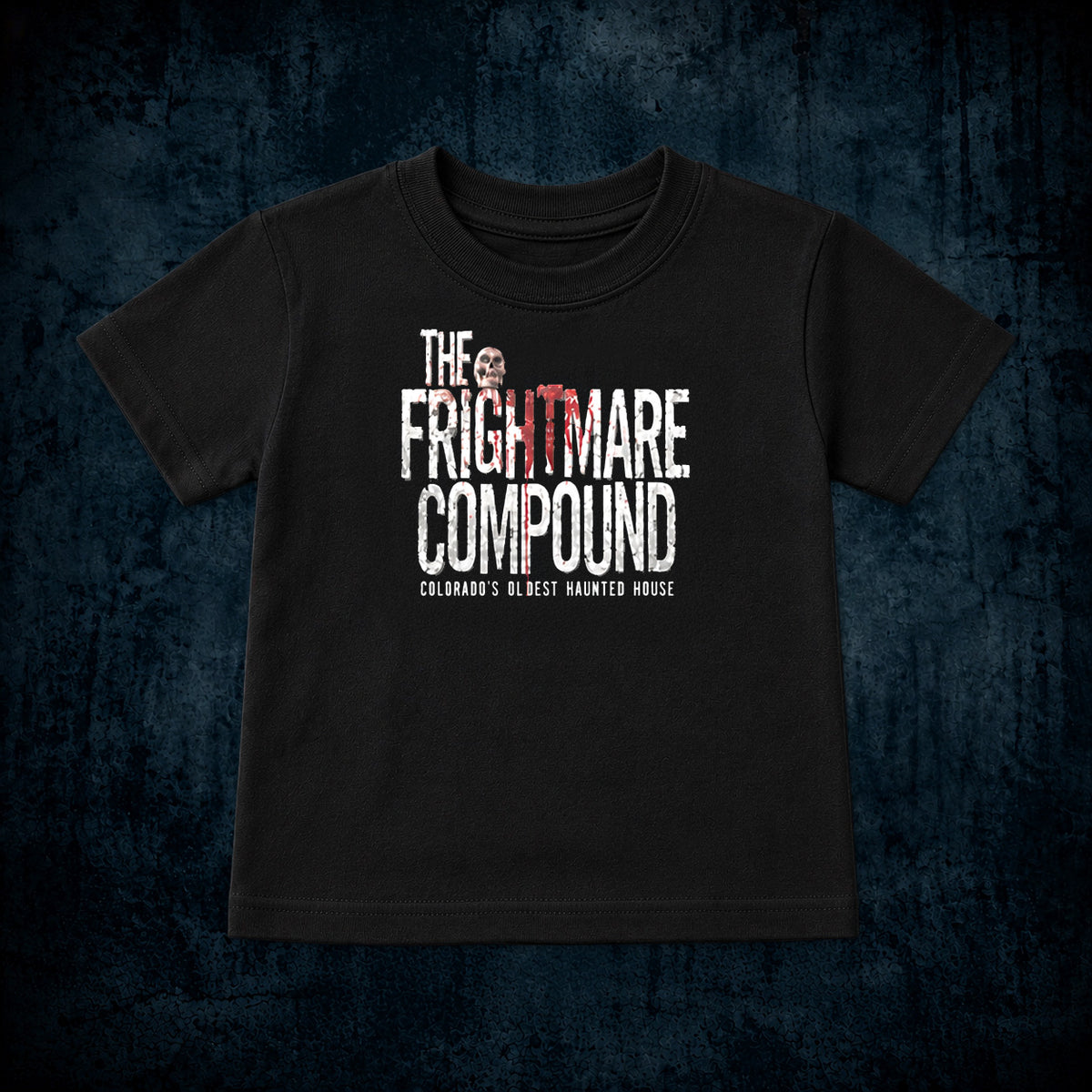 A black short-sleeve t-shirt with a distressed graphic reading 'THE FRIGHTMARE COMPOUND' in white and red, plus smaller text 'COLORADO'S OLDEST HAUNTED HOUSE', shown on a dark textured blue background.