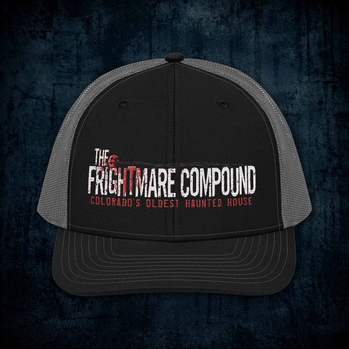 A black and gray trucker hat with a printed graphic on the front reading 'The Frightmare Compound' and 'Colorado's Oldest Haunted House' in white and red, shown against a dark textured background.